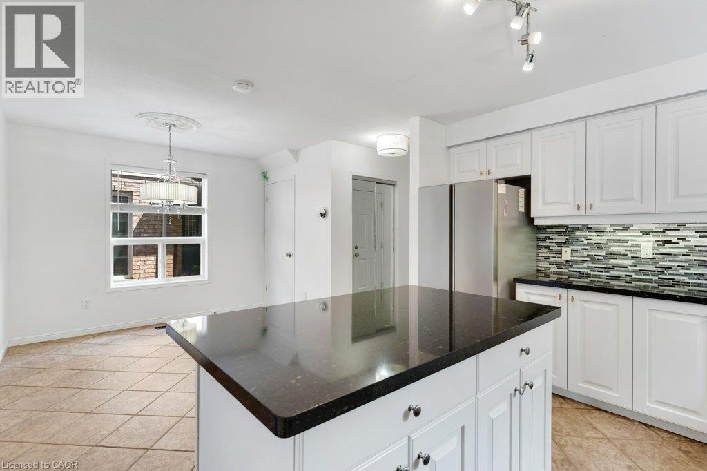 Kitchen featuring a central island with a dark countertop, white cabinetry with gold-tone hardware, and a mosaic tile backsplash - 76 Renner Drive, Cambridge, ON - Indoor Photo Showing Kitchen With Upgraded Kitchen