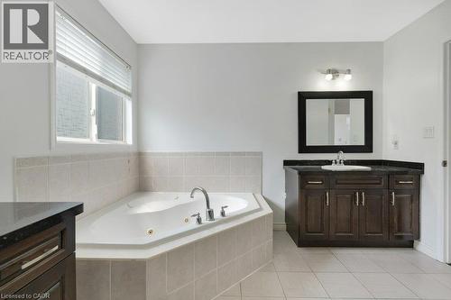 Soaking tub with tiled surround, wood-finish vanity with countertop, and large framed mirror - 76 Renner Drive, Cambridge, ON - Indoor Photo Showing Bathroom