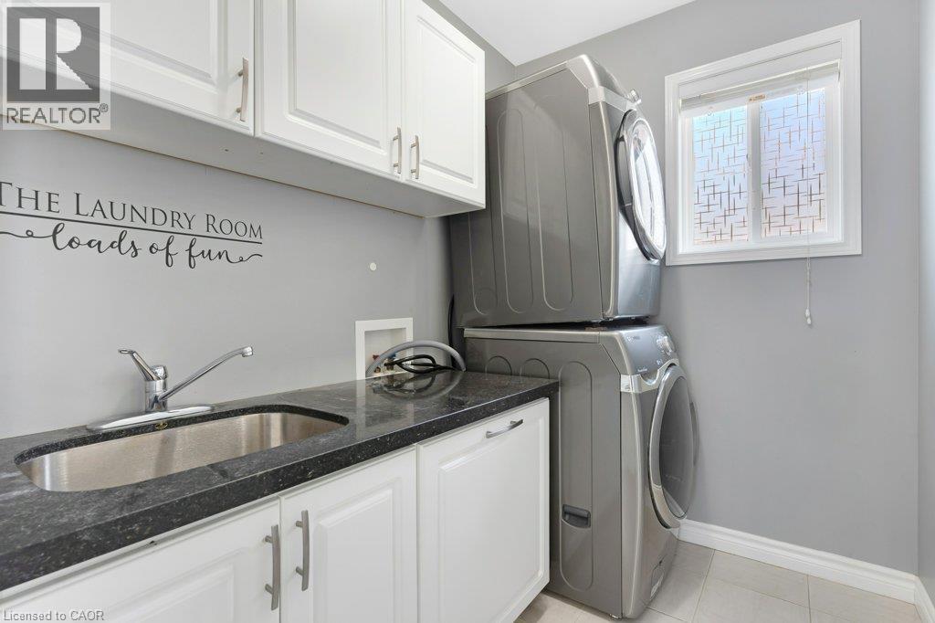 Laundry room featuring a stainless steel sink, dark countertop, white cabinetry with silver hardware, and a window with patterned film - 76 Renner Drive, Cambridge, ON - Indoor Photo Showing Laundry Room