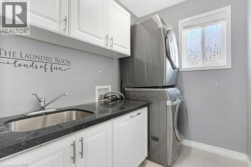 Laundry room featuring a stainless steel sink, dark countertop, white cabinetry with silver hardware, and a window with patterned film - 76 Renner Drive, Cambridge, ON - Indoor Photo Showing Laundry Room