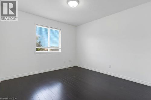 Bright interior with a window featuring horizontal blinds, dark wood-finish flooring, white walls, and a ceiling-mounted light fixture - 76 Renner Drive, Cambridge, ON - Indoor Photo Showing Other Room