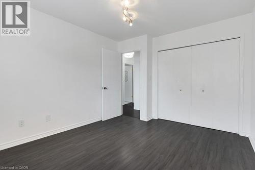 Dark wood-finish flooring with white baseboards, a white interior door, and double bi-fold closet doors - 76 Renner Drive, Cambridge, ON - Indoor Photo Showing Other Room