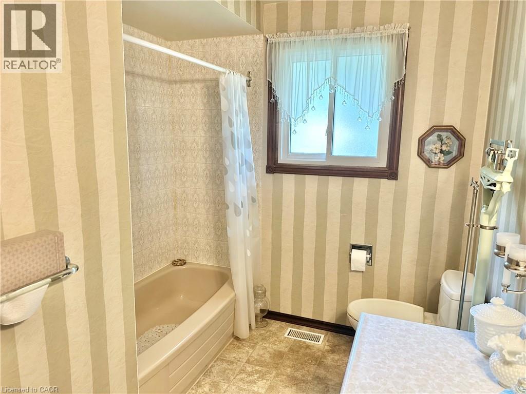 Bathroom featuring a built-in bathtub, a window with a wood-finish frame, and striped wallpaper - 44 Douglas Avenue, Simcoe, ON - Indoor Photo Showing Bathroom