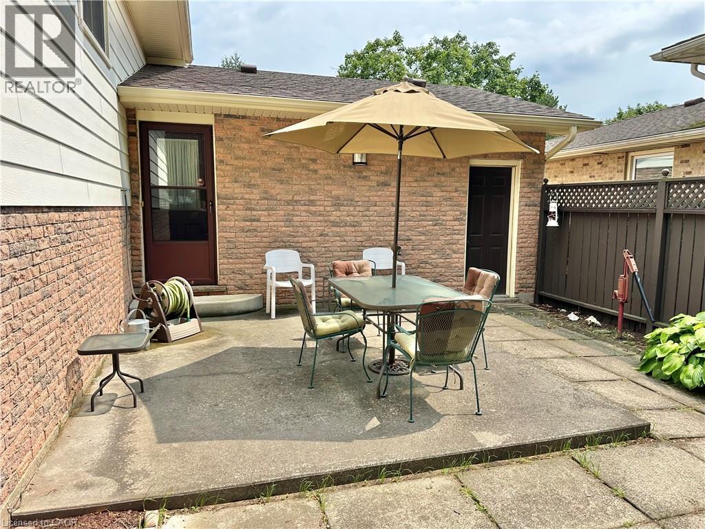 Expansive concrete patio area with a privacy fence and exterior brick walls - 44 Douglas Avenue, Simcoe, ON - Outdoor With Exterior