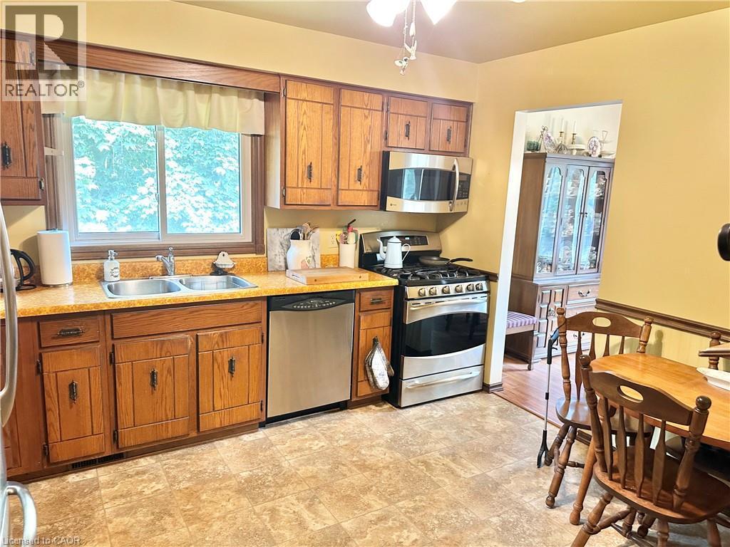 Wood-finish cabinetry, stainless steel dishwasher, stainless steel gas range with overhead microwave, and a double basin sink - 44 Douglas Avenue, Simcoe, ON - Indoor Photo Showing Kitchen With Double Sink