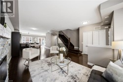 Open-concept living space featuring dark wood-finish flooring, a stone-faced fireplace, recessed lighting, and a staircase with dark wood treads - 