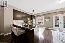 Open-concept kitchen featuring dark wood cabinetry, stainless steel appliances, a textured tile backsplash, and a breakfast bar with stone-finish countertop - 