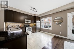 Kitchen featuring dark wood cabinetry, stainless steel appliances, dark stone countertops, tile backsplash, and mixed flooring - 