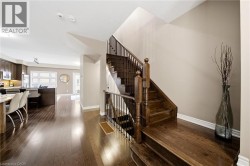 Dark wood-finish flooring, staircase with dark wood treads and railings, recessed ceiling lighting, and a kitchen with dark wood cabinetry - 