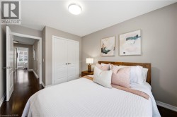 Serene primary bedroom featuring warm wood-finish bed frame, soft neutral wall palette, recessed ceiling lighting, and coordinating artwork - 