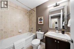 Spa-inspired bathroom featuring a soaking tub with tile surround, dual vanity with stone countertop and dark cabinetry, framed mirror with integrated lighting, and a separate toilet compartment - 