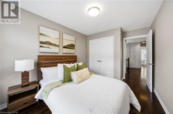 Inviting bedroom showcasing warm wood-finish flooring, a rich wood-stframe bed with upholstered headboard, coordinated bedding with decorative pillows, paired wood nightstands with integrated task lig - 