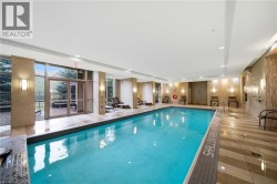 Indoor swimming pool with full-height exterior windows, recessed ceiling lighting, wall-mounted sconces, and patterned floor tiling - 