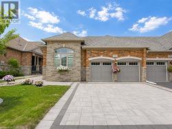 Brick and stone facade, arched window detailing, three garage bays, paver driveway, and manicured lawn - 