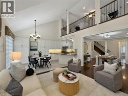 Vaulted ceiling with chandelier, white cabinetry, kitchen island with built-in appliances, dark wood-finish flooring, and an open loft area with iron railings - 