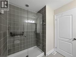 Glass-enclosed shower with gray square tile surround, a built-in shower caddy, and a white shower base - 