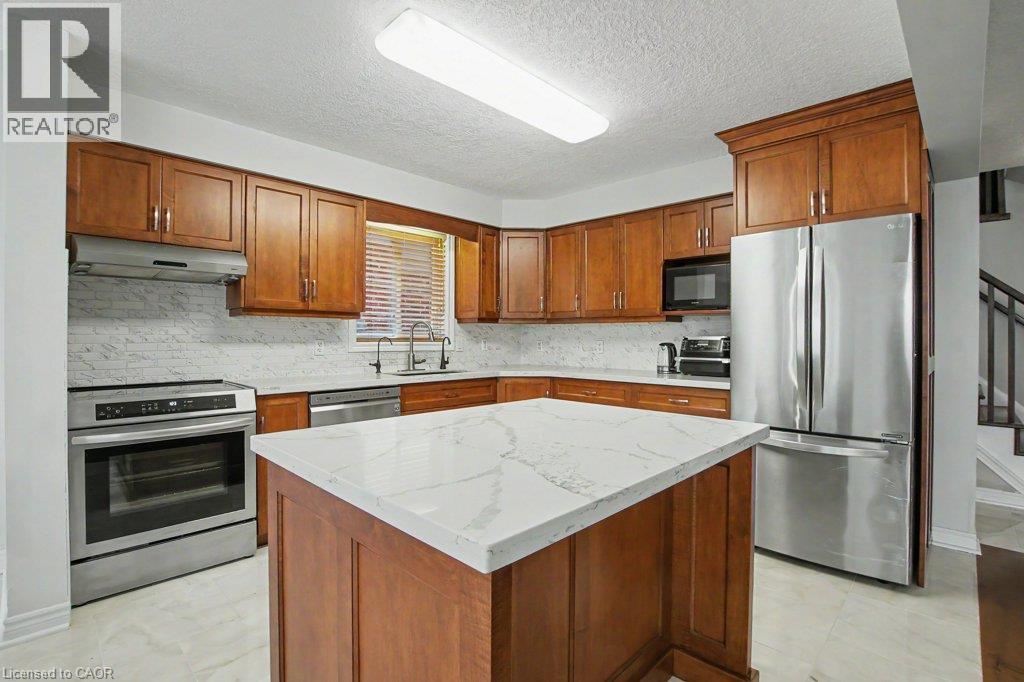 Kitchen featuring a central island with a quartz countertop, Maple wood cabinetry, stainless steel appliances, and a tiled backsplash - 568 Robert Ferrie Drive, Kitchener, ON - Indoor Photo Showing Kitchen