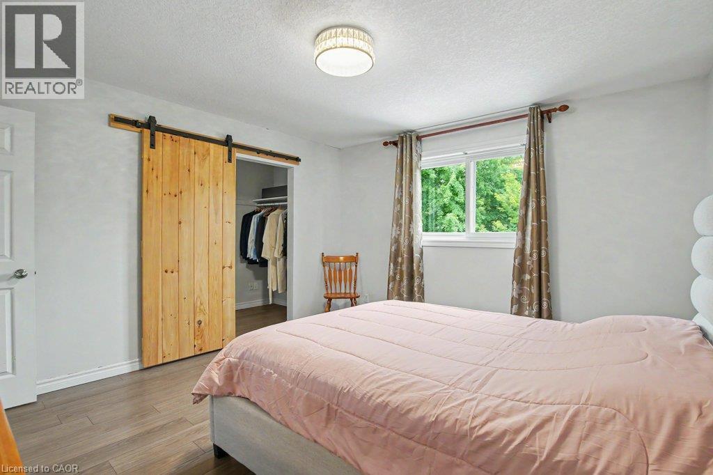 Wood finished flooring throughout, featuring a natural wood barn door, a walk-in closet with shelving and an ensuite bathroom - 568 Robert Ferrie Drive, Kitchener, ON - Indoor Photo Showing Bedroom