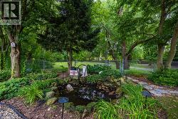 Landscaped yard featuring a rock-lined pond, mature trees, and a chain-link fence - 