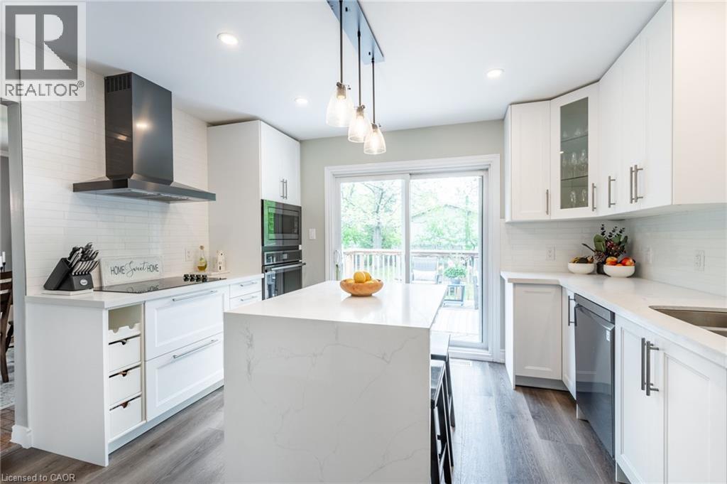 White shaker-style cabinetry, a contrasting dark range hood, a kitchen island with a white countertop, stainless steel appliances, and a glass sliding door - 152 Concession 7 Road E, Millgrove, ON - Indoor Photo Showing Kitchen With Upgraded Kitchen