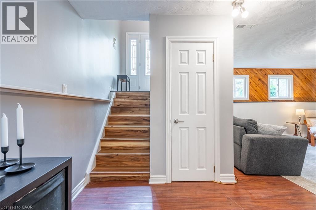 Wood-finish flooring, staircase with wood treads, white panel door, white trim, and two square windows with wood paneling - 152 Concession 7 Road E, Millgrove, ON - Indoor Photo Showing Other Room