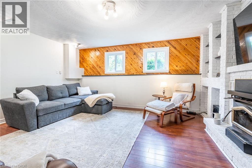 Warm wood-finish flooring, white painted brick fireplace with built-in shelving, two windows for natural light, and wood paneling accent wall - 152 Concession 7 Road E, Millgrove, ON - Indoor Photo Showing Living Room With Fireplace