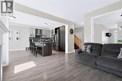 Open-concept living space featuring wood-finish flooring, a modern kitchen with an island, and stainless steel appliances - 