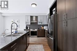 Contemporary kitchen featuring wood-finish flooring, stainless steel appliances, dark wood-finish cabinetry, and a double basin sink with a high-arc faucet - 