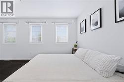 Spacious room with white walls, dark carpet, and three windows featuring white blinds and black curtain rods - 