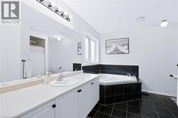 Elongated vanity with an integrated sink and storage cabinetry, large wall-mounted mirror, corner soaking tub with black tile surround, and black tile flooring - 
