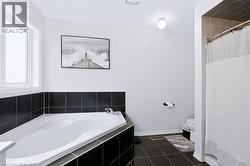 Corner soaking tub with dark tile surround, light wall paint, and dark tile flooring - 