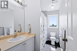 Vanity with integrated sink and countertop, white cabinetry with silver hardware, large wall-mounted mirror, and a window in the shower area - 