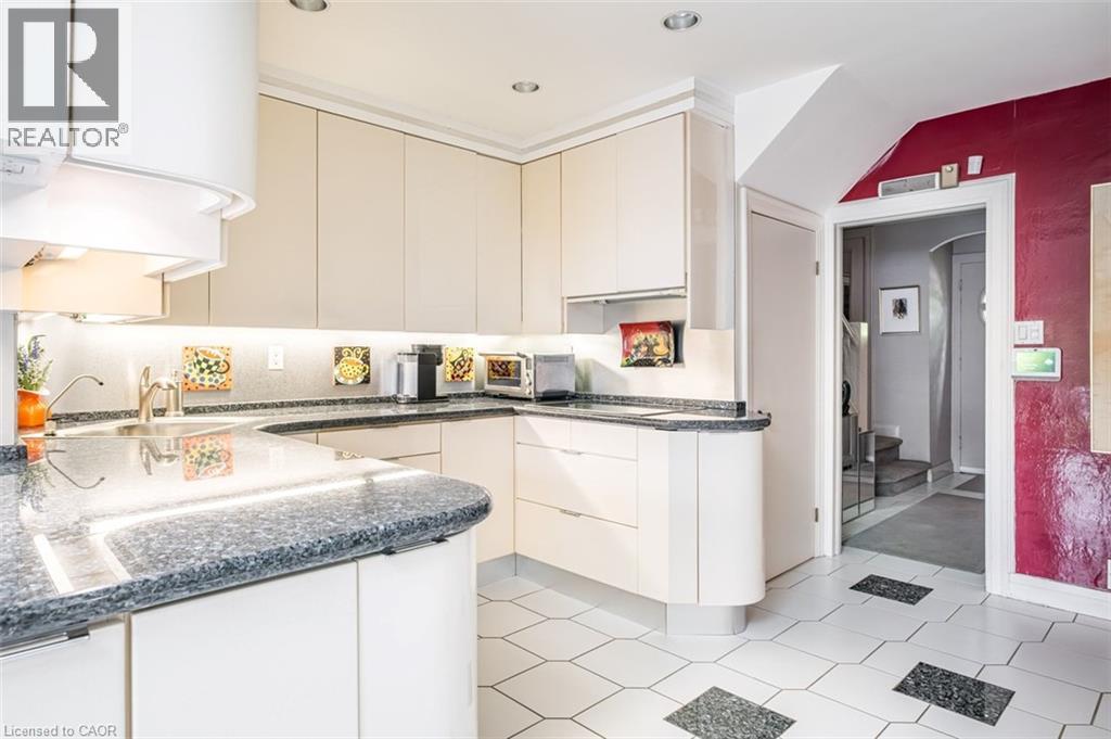 Kitchen featuring light-toned cabinetry, dark speckled countertops, under-cabinet lighting, a stainless steel sink, and geometric floor tiling - 107 Bond Street S, Hamilton, ON - Indoor Photo Showing Kitchen