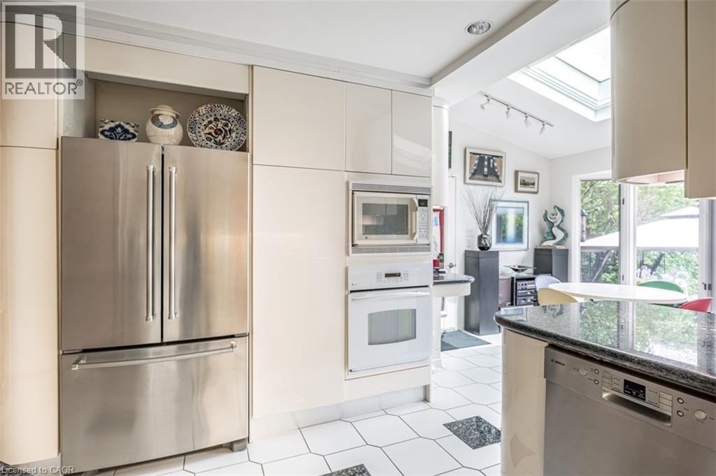 Kitchen featuring stainless steel refrigerator, integrated microwave and oven, built-in dishwasher, black granite-style countertops, and white hexagon tile flooring with dark accent tiles - 107 Bond Street S, Hamilton, ON - Indoor Photo Showing Kitchen