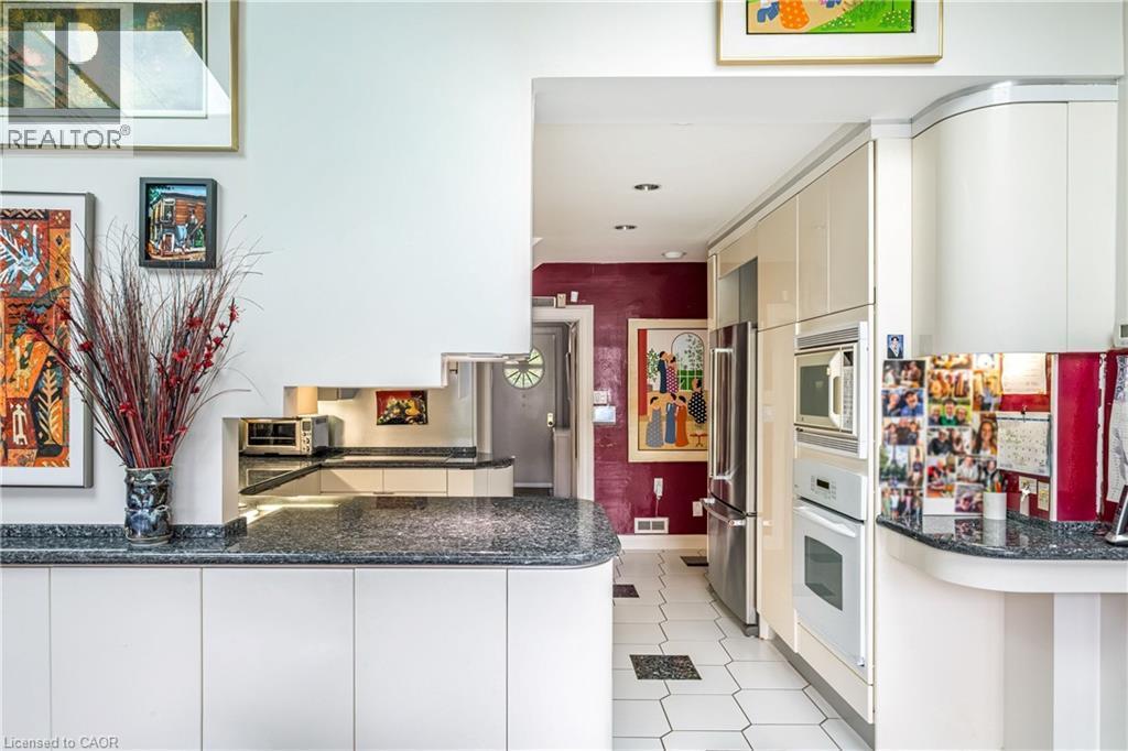 Built-in stainless steel appliances, granite-look countertops, white cabinetry with integrated handles, and hexagonal floor tiling - 107 Bond Street S, Hamilton, ON - Indoor