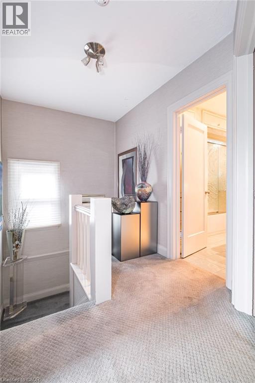Light gray wall-to-wall carpeting, white painted stair railing, natural light from a window with blinds, and white trim throughout - 107 Bond Street S, Hamilton, ON - Indoor