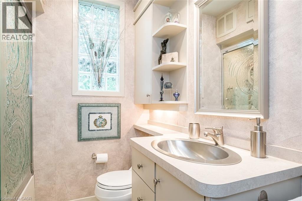 Vanity with integrated sink, built-in shelving, cabinet storage, and a glass block window - 107 Bond Street S, Hamilton, ON - Indoor Photo Showing Bathroom