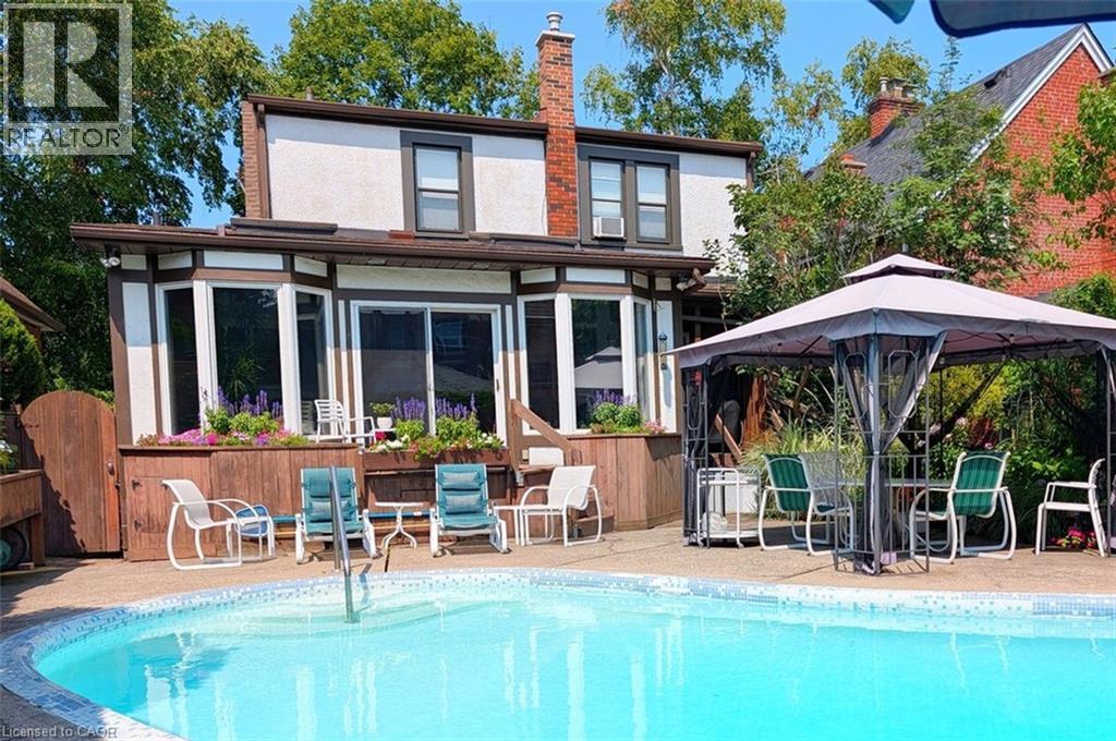 Rear exterior featuring a swimming pool, expansive patio, and a second-story bay window - 107 Bond Street S, Hamilton, ON - Outdoor With In Ground Pool
