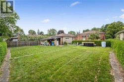 Expansive rear grounds featuring a meticulously manicured lawn with mature tree-lined perimeter, brick paver pathways, and established hedging - 