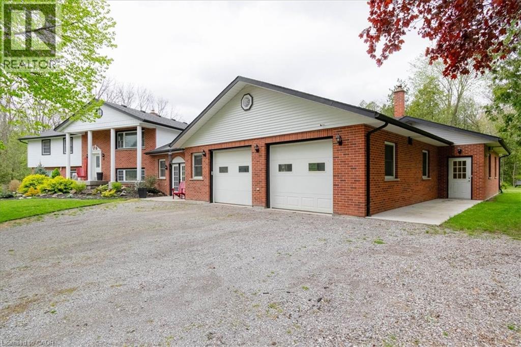Brick and white siding exterior featuring a two-car garage with white paneled doors, a covered front entry with columns, and a large gravel driveway - 111 Decou Road, Simcoe, ON - Outdoor