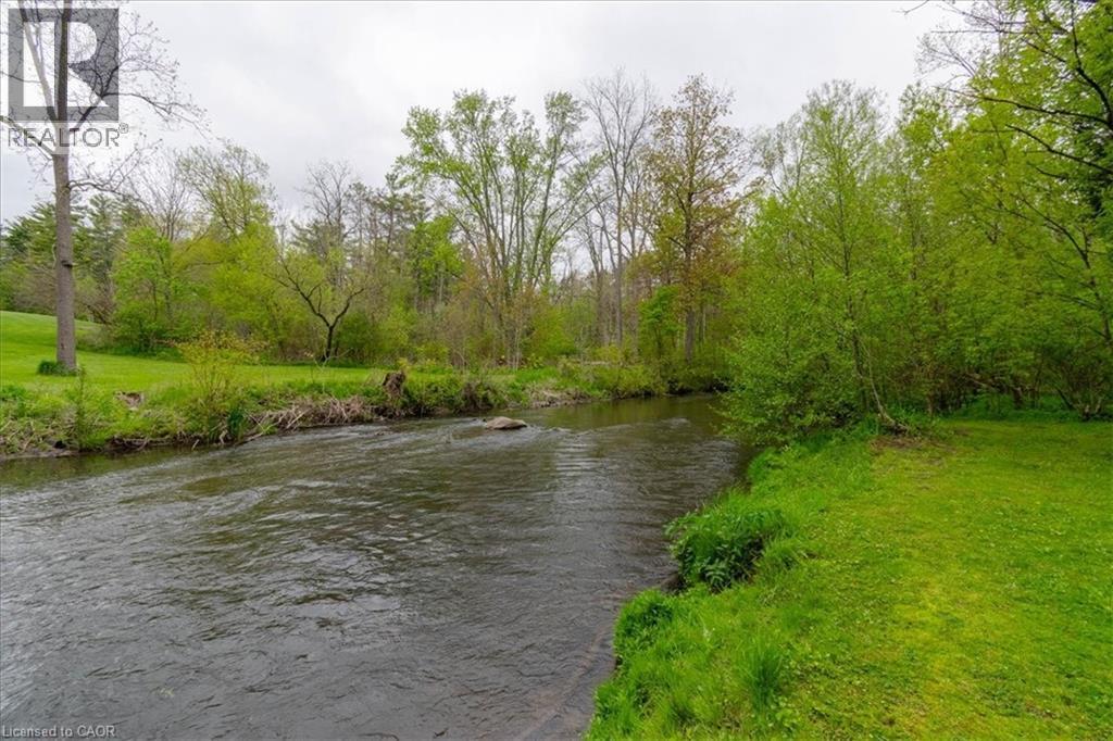 Waterfront property featuring a flowing river, lush green grass, mature trees, and natural landscaping - 111 Decou Road, Simcoe, ON - Outdoor With Body Of Water