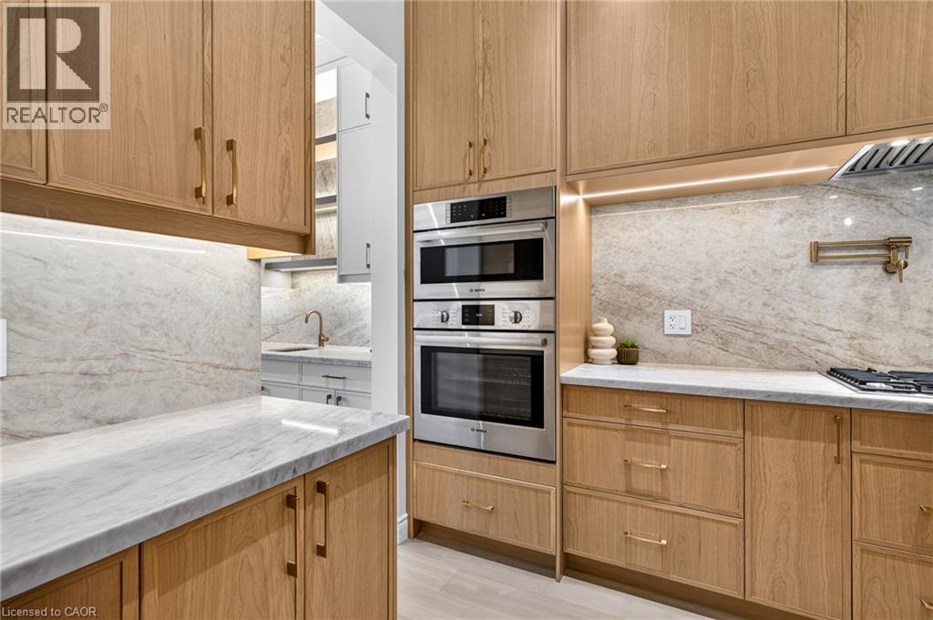 Wood-finish cabinetry, light-toned stone countertops, integrated stainless steel appliances, stone backsplash, and recessed under-cabinet lighting - 67 Cielo Court, Hamilton, ON - Indoor Photo Showing Kitchen