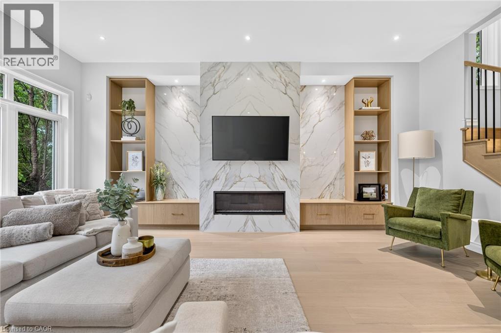 Marble-look fireplace surround with an integrated linear electric fireplace, custom built-in shelving, wood-finish flooring, and recessed lighting - 67 Cielo Court, Hamilton, ON - Indoor Photo Showing Living Room With Fireplace
