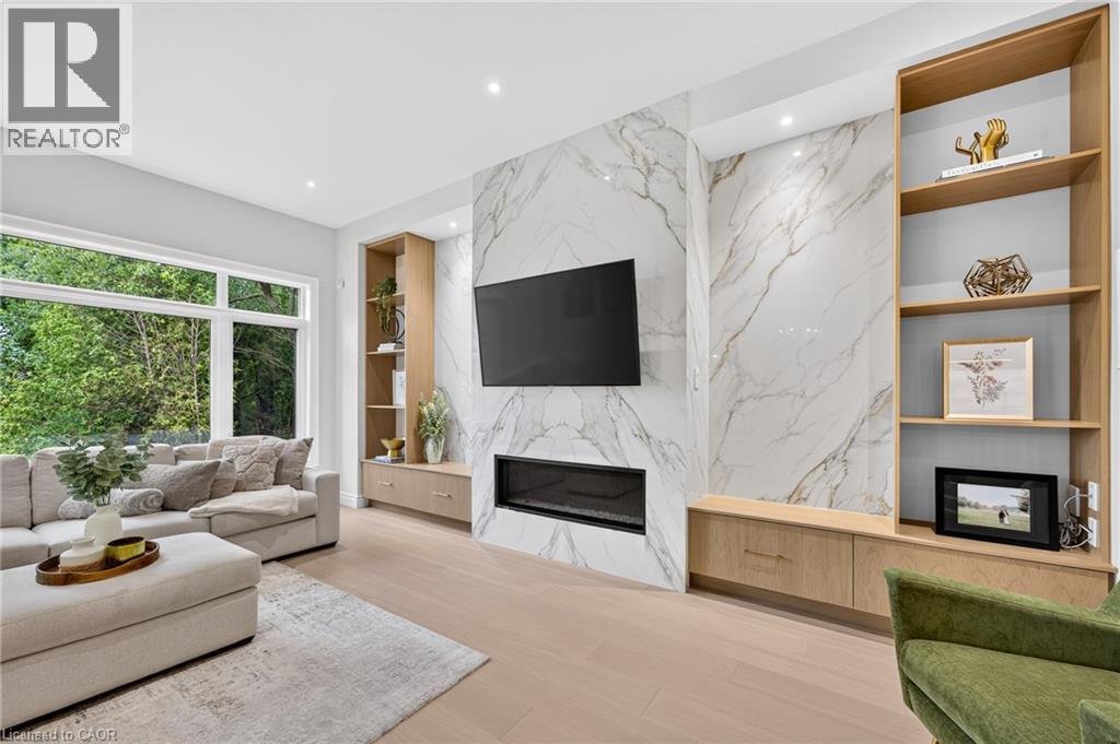 Modern living space featuring an expansive window, light wood-finish flooring, a contemporary fireplace, and built-in shelving with integrated cabinetry - 67 Cielo Court, Hamilton, ON - Indoor Photo Showing Living Room With Fireplace