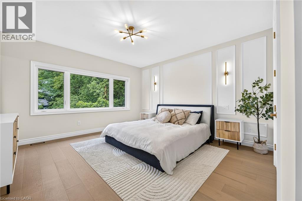 Expansive window providing abundant natural light, wood-finish flooring, accent wall paneling, and modern light fixtures - 67 Cielo Court, Hamilton, ON - Indoor Photo Showing Bedroom