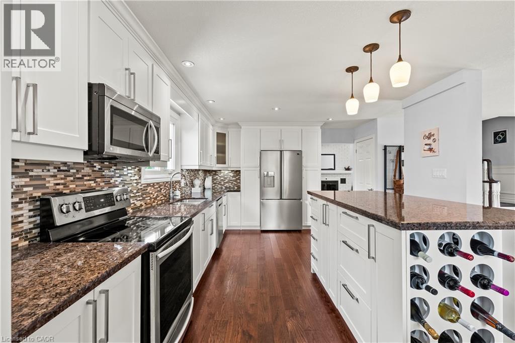 White shaker-style cabinetry, stainless steel appliances, wood-finish flooring, granite countertops, and a mosaic tile backsplash - 87 Monte Drive, Hamilton, ON - Indoor Photo Showing Kitchen With Stainless Steel Kitchen With Upgraded Kitchen