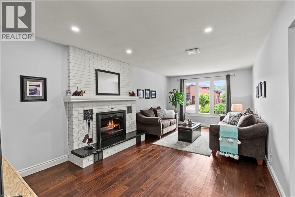 Living area featuring wood-finish flooring, a white brick fireplace with a dark hearth, and recessed ceiling lighting - 87 Monte Drive, Hamilton, ON - Indoor Photo Showing Living Room With Fireplace