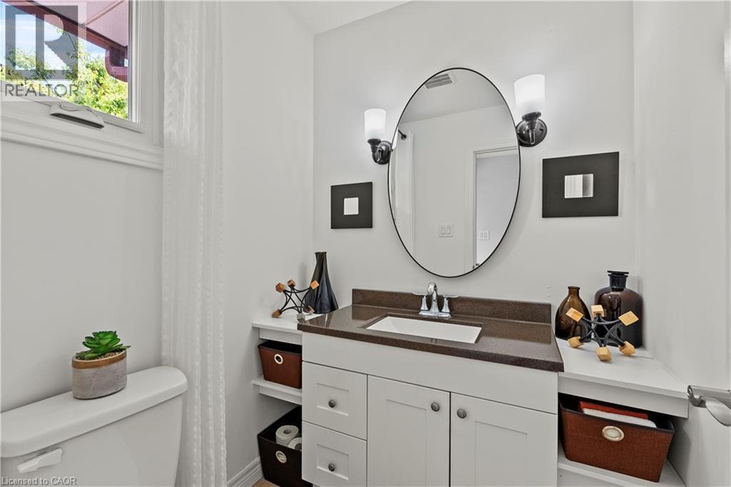 White vanity with a brown countertop, integral rectangular sink, oval mirror, and wall-mounted sconces - 87 Monte Drive, Hamilton, ON - Indoor Photo Showing Bathroom