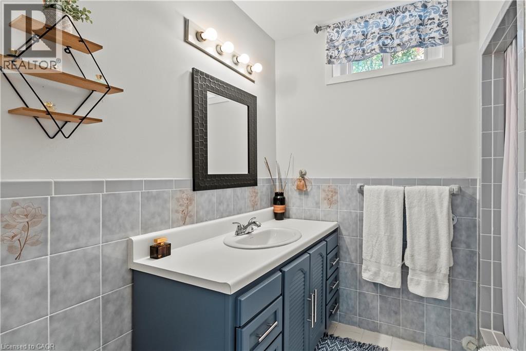 Vanity with integrated sink, patterned wall tiling, framed mirror, and upper wall-mounted lighting fixture - 87 Monte Drive, Hamilton, ON - Indoor Photo Showing Bathroom