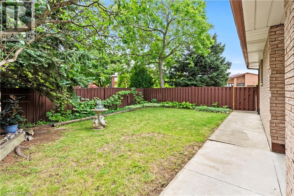 Private fenced yard with mature trees, established perennial plantings, and a concrete pathway - 87 Monte Drive, Hamilton, ON - Outdoor